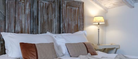 Una cama con almohadas blancas y marrones, una lámpara y un cabecero de madera rústica.
