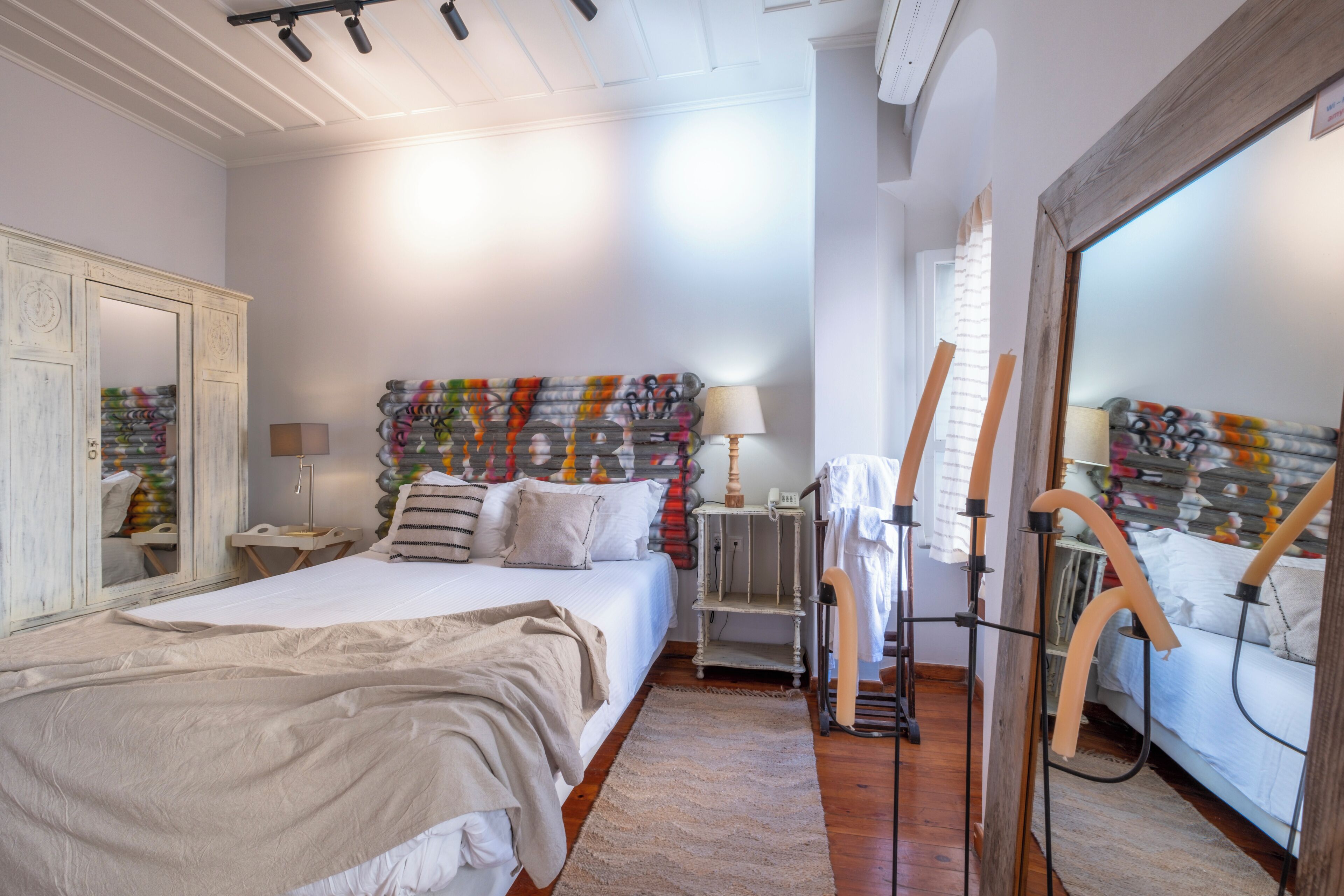 A bedroom with a bed, a dresser, a mirror, a lamp, and a colorful headboard.