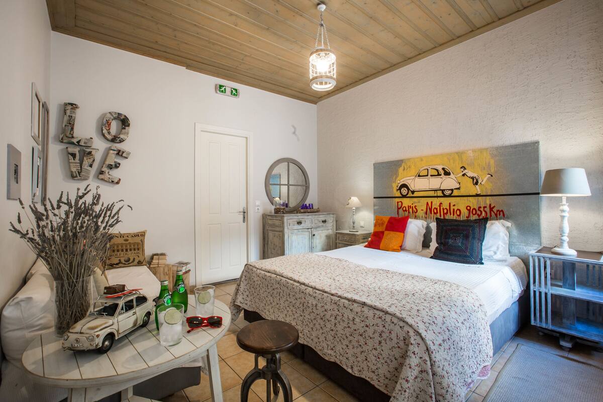 A bedroom with a bed, a desk with a car model, a lamp, and a painting on the wall.