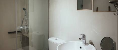 A bathroom with a glass-enclosed shower, a white sink, and a mirror.