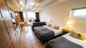 Hotellihuone, jossa on kaksi sänkyä, pieni työpöytä, televisio ja parveke, jolta on näkymä.