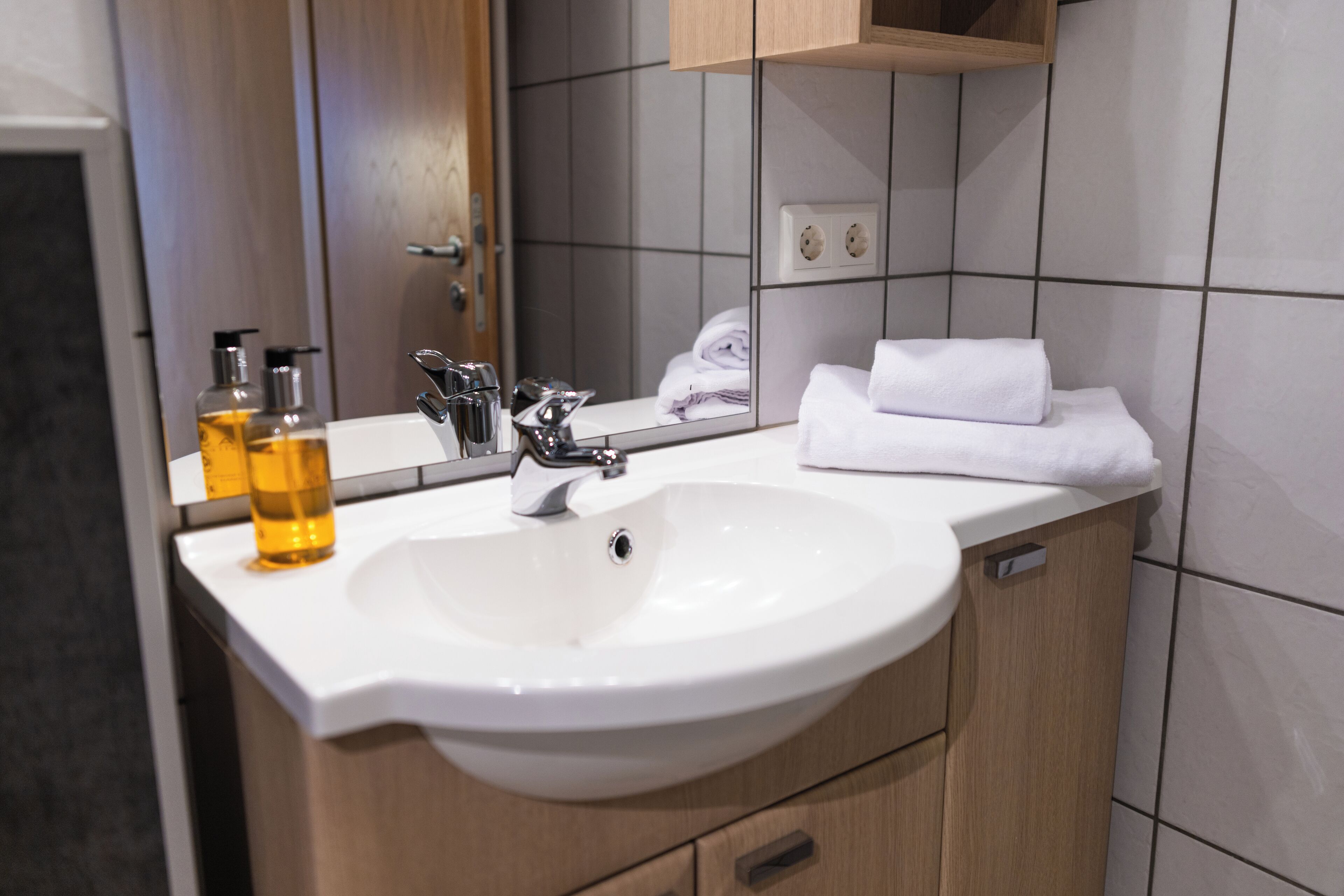 A modern bathroom with a white sink, a mirror, and a wooden cabinet.