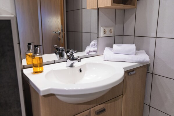 A modern bathroom with a white sink, a mirror, and a wooden cabinet.