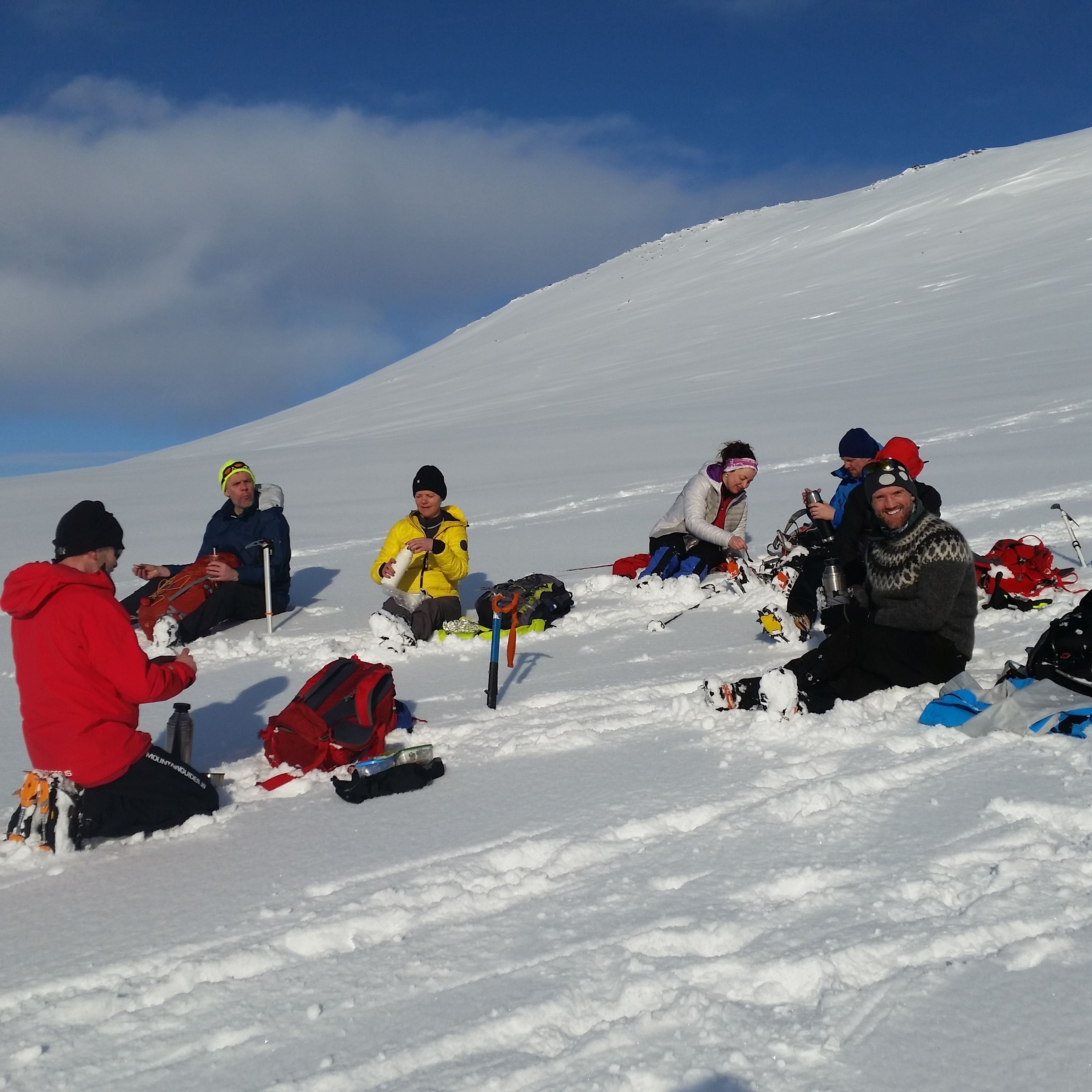 Un grupo de personas sentadas en una ladera cubierta de nieve, rodeadas de su equipo.