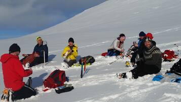 Un grupo de personas sentadas en una ladera cubierta de nieve, rodeadas de su equipo.