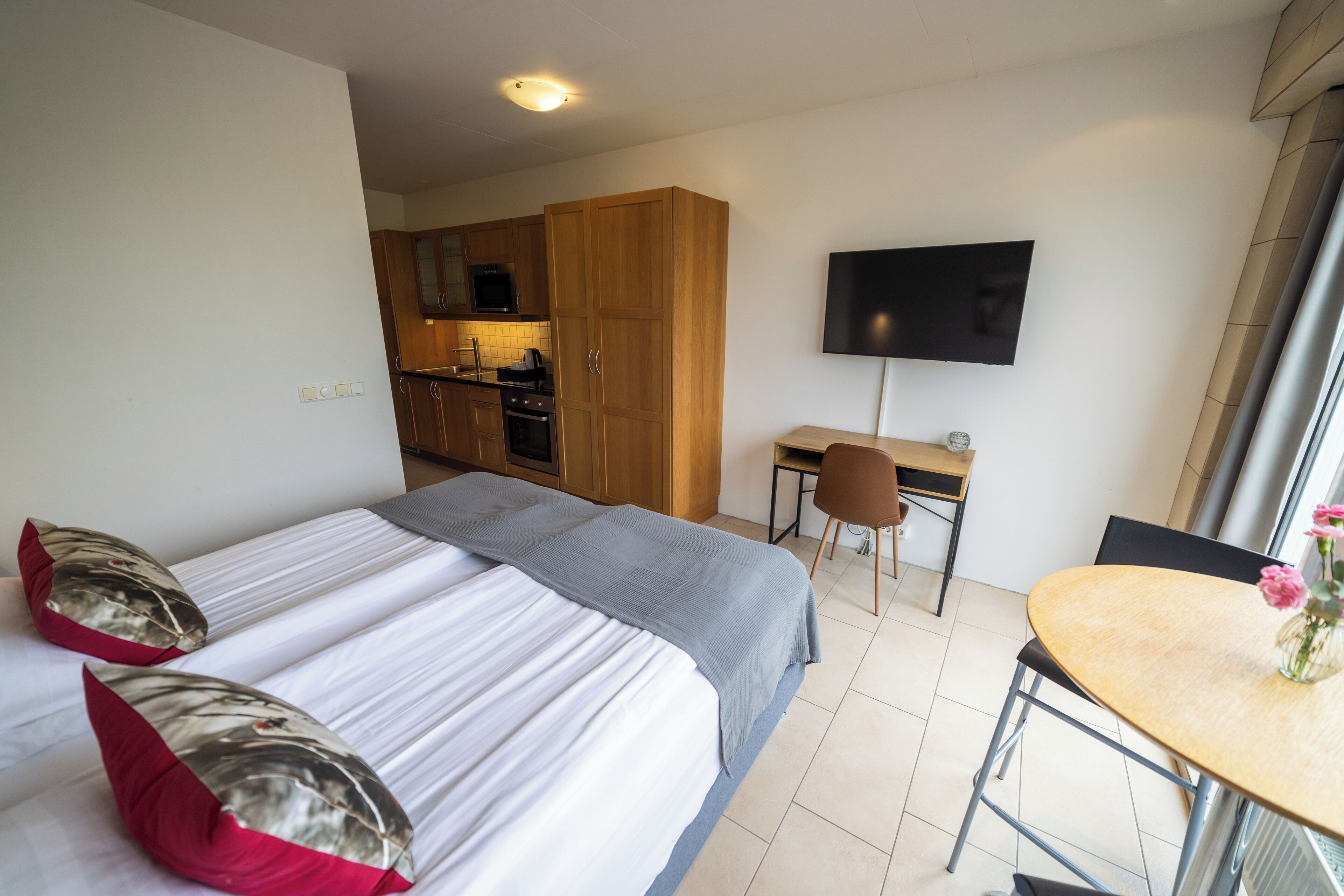 Habitación de hotel con dos camas, un escritorio, una silla, un televisor y una zona de cocina.