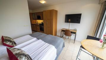Habitación de hotel con dos camas, un escritorio, una silla, un televisor y una zona de cocina.