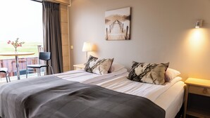 Hotellihuone, jossa on suuri sänky, kaksi yöpöytää, tuoli, lamppu ja taulu seinällä.