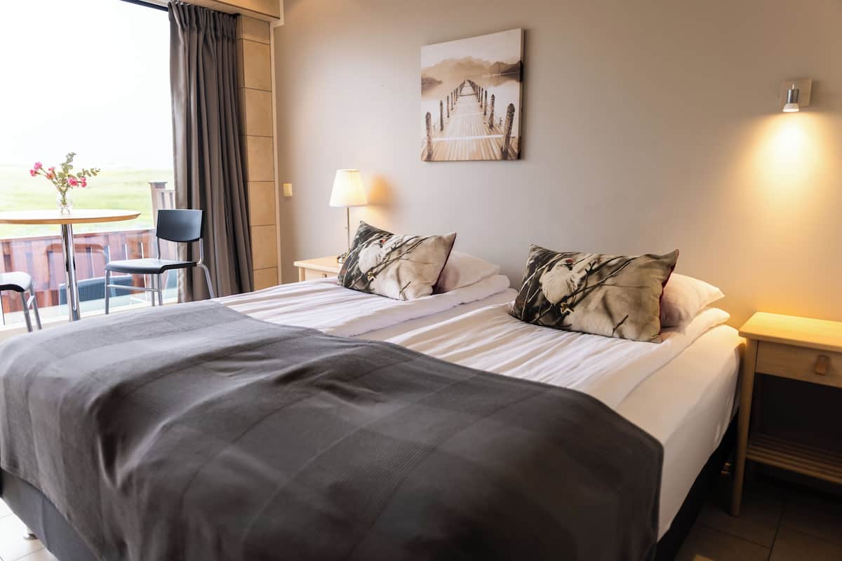 Ein Hotelzimmer mit einem großen Bett, zwei Nachttischen, einem Sessel, einer Lampe und einem Bild an der Wand.