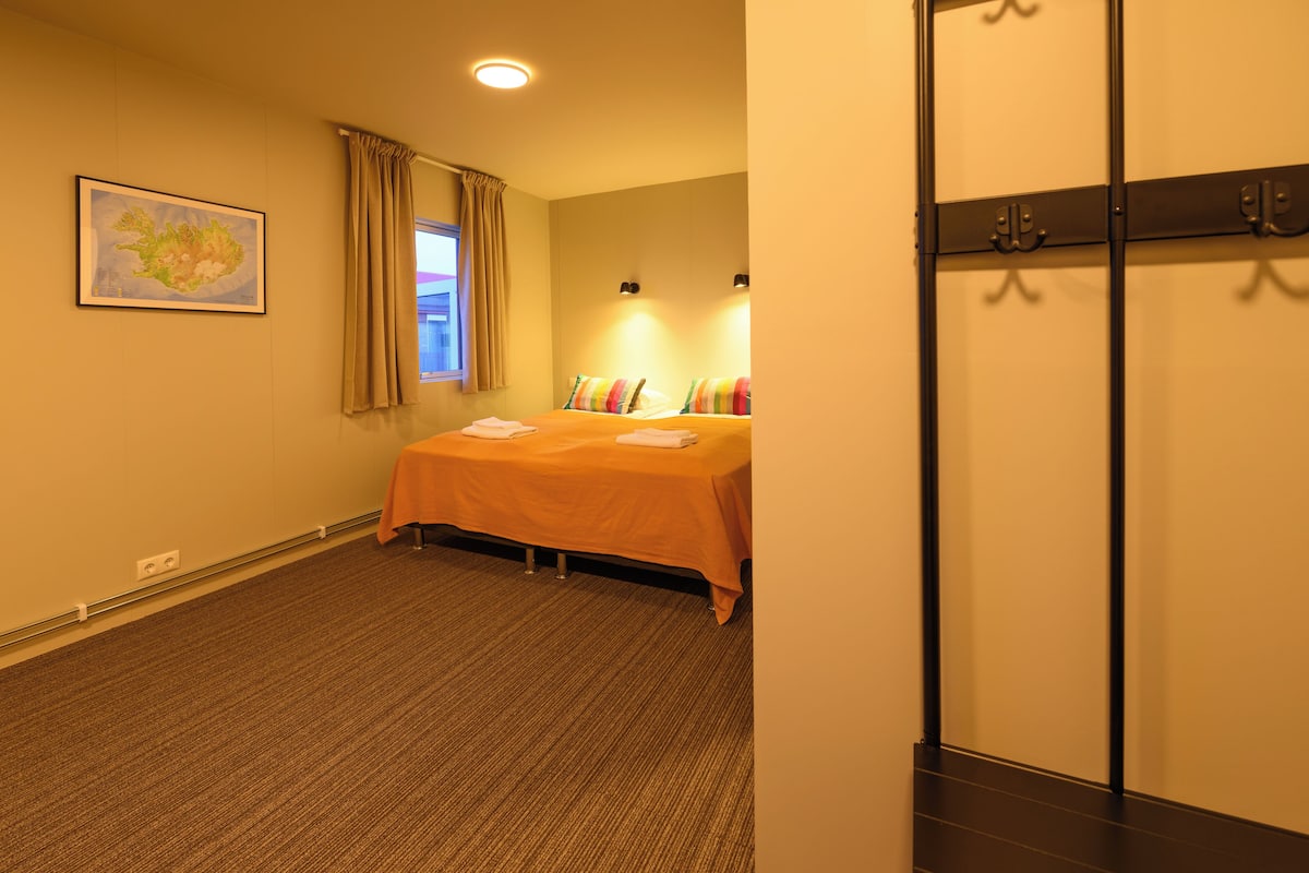 Ein Hotelzimmer mit Bett, Fenster mit Vorhängen, Wandleuchte und Kleiderhaken.