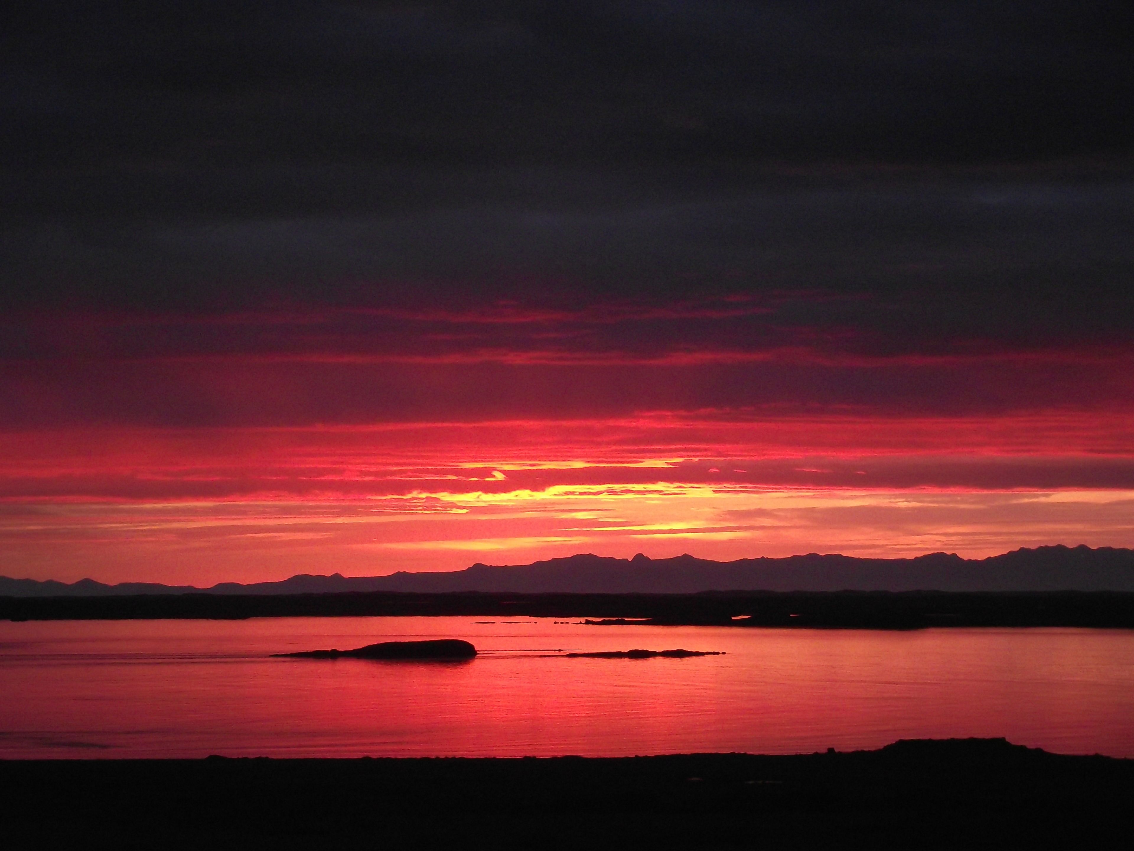 A sunset over a calm body of water with silhouettes of mountains in the background.