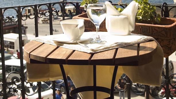 Un balcón con una mesa lista para comer, con vista a un cuerpo de agua y un paisaje montañoso.