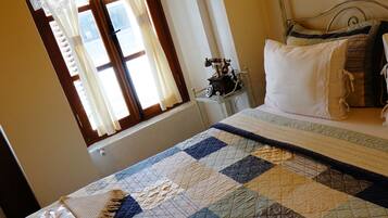 A neatly made bed with a quilt, a nightstand with a lamp, and a window with curtains.