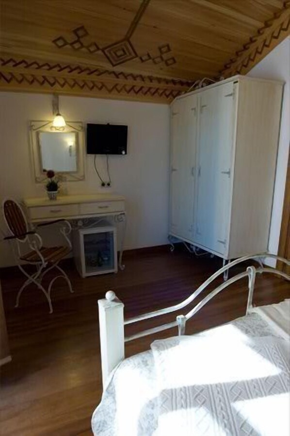 A bedroom with a wooden ceiling, a bed, a desk with a chair, a wardrobe, and a mirror.
