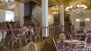 Un vestíbulo de hotel con una escalera de madera, sillas de metal blanco y candelabros.