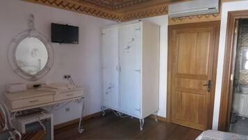 A room with a wooden door, a white wardrobe, a mirror, a small desk with a chair, and a television mounted on the wall.