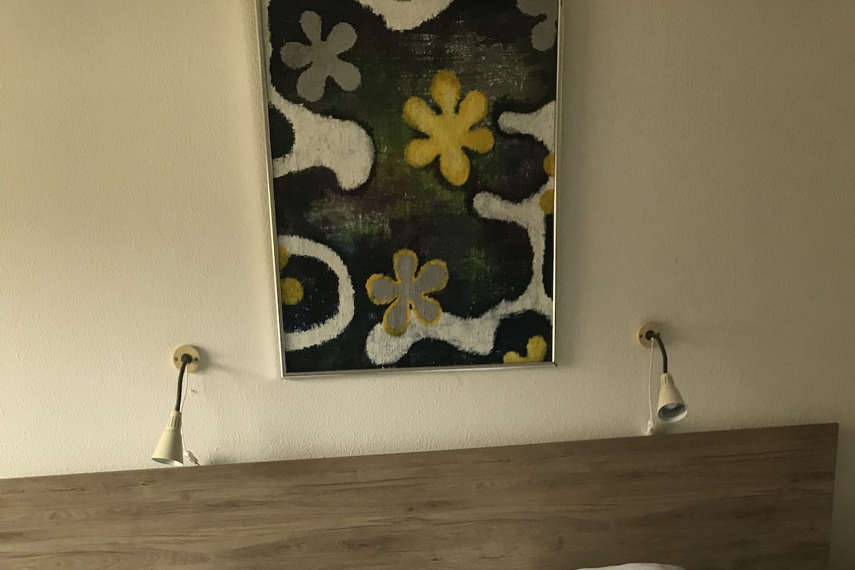 A hotel room with two single beds, a wooden headboard, a wall-mounted painting, and two bedside lamps.