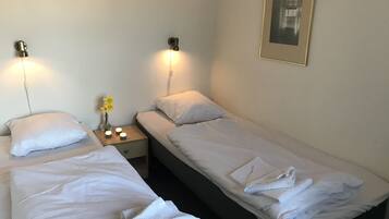 A hotel room with two single beds, a nightstand with a vase of flowers, and wall-mounted lights.