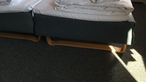 Una cama doble con ropa de cama blanca, dos lámparas de noche, un cuadro abstracto enmarcados y un florero con flores amarillas sobre una mesita de noche.