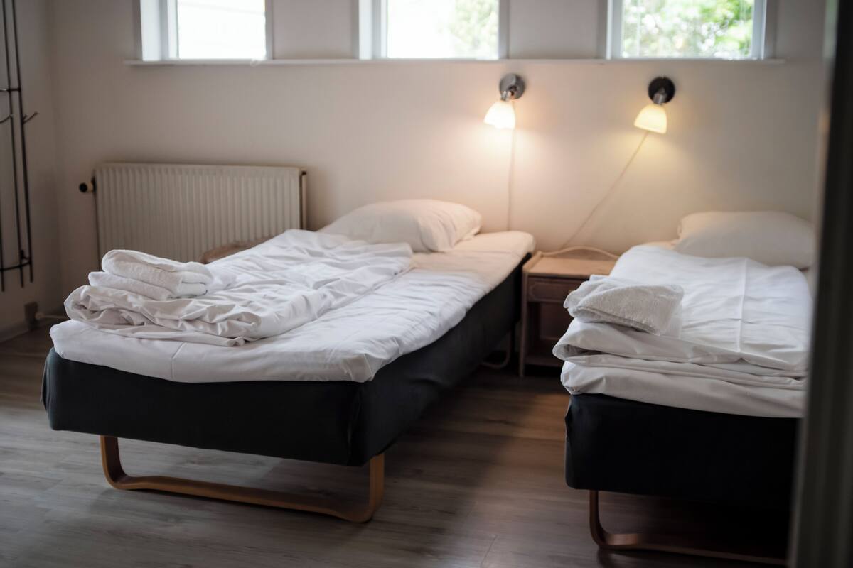 A bedroom with two beds, a radiator, and two bedside lamps.