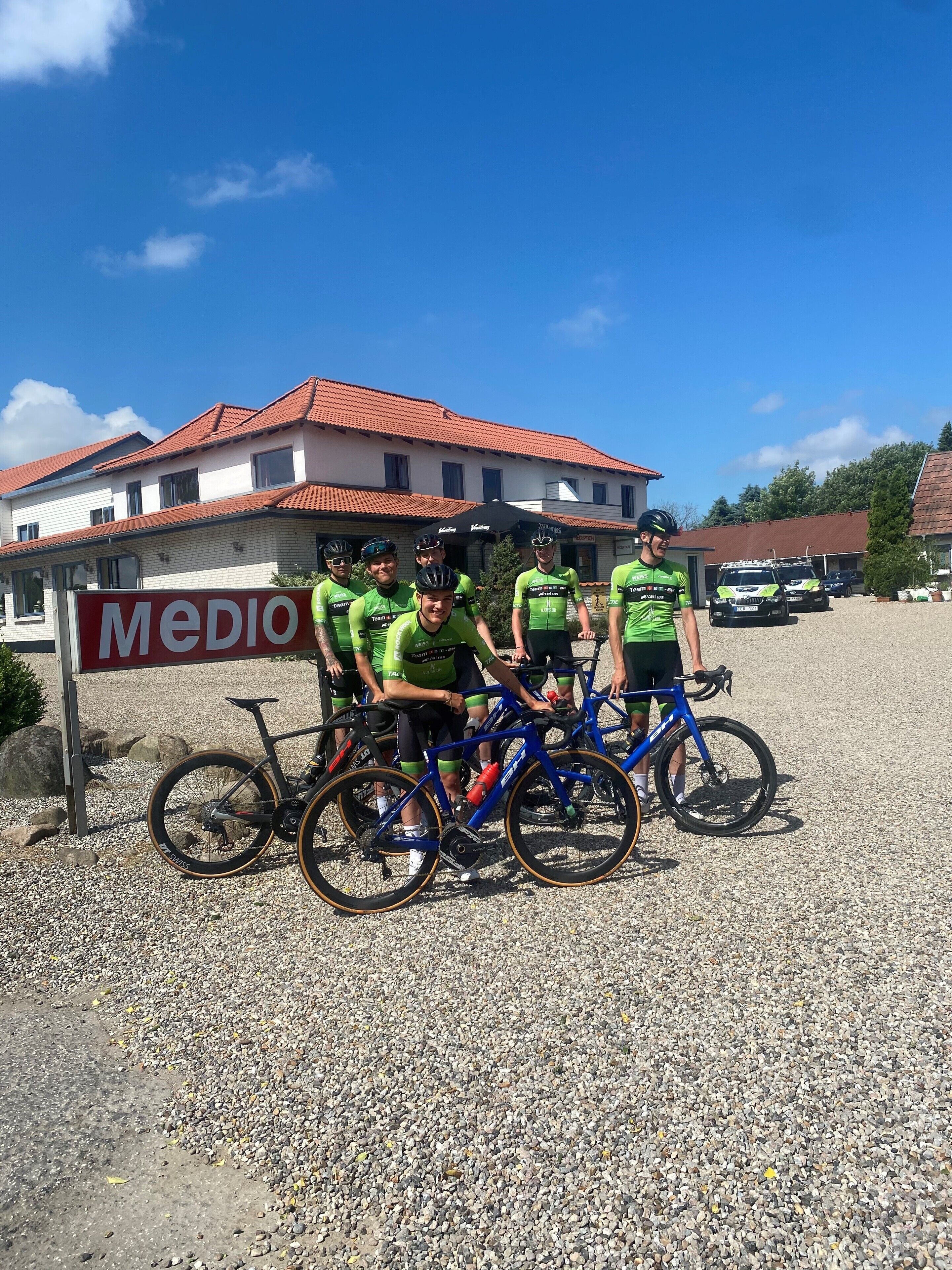 A group of cyclists in front of a building with a sign that reads 'MEDIO'.
