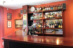 A bar with shelves of liquor bottles and glasses, a clock, and framed pictures on the wall. - Hotel Medio (Fredericia)
