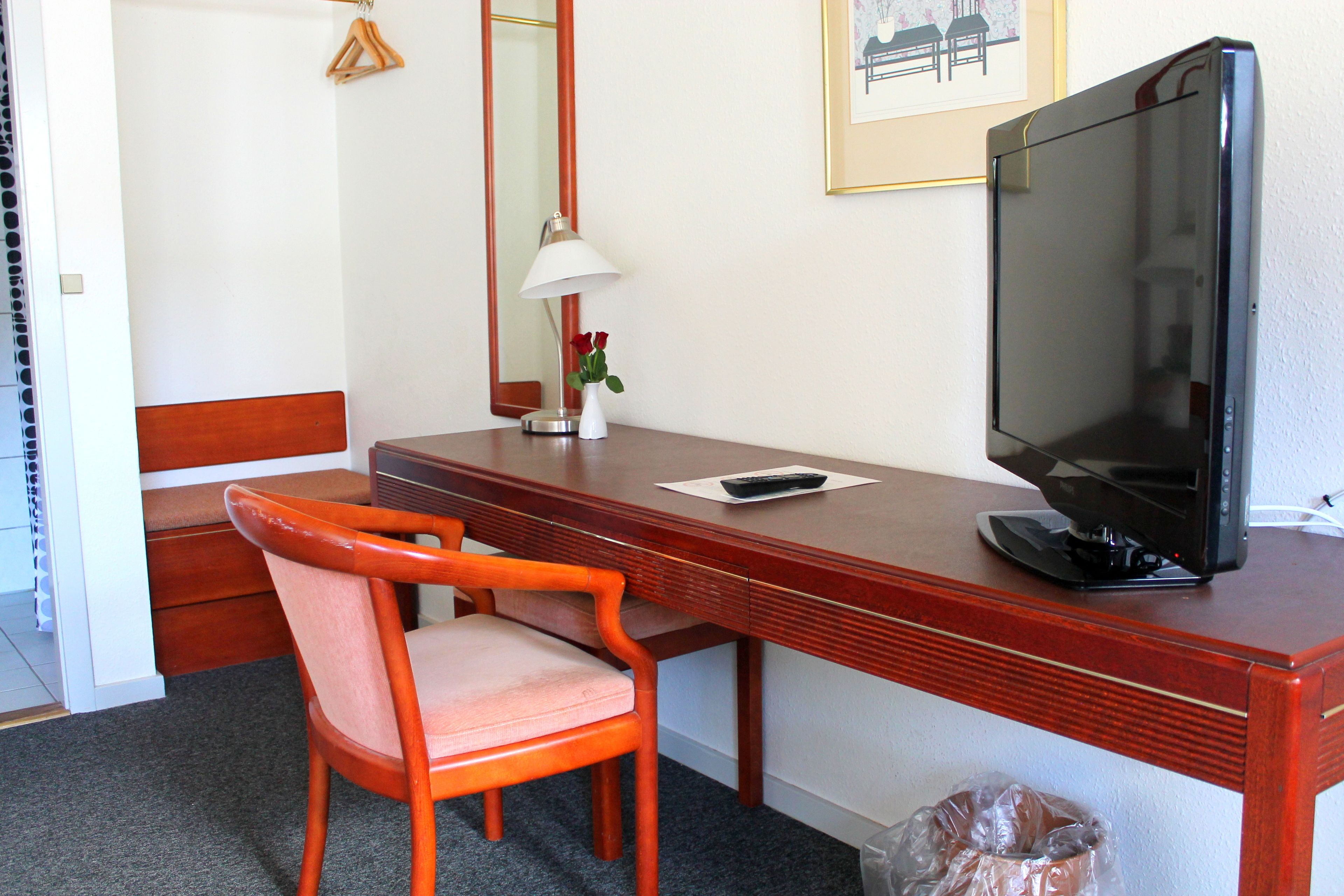 A hotel room with a wooden desk, a chair, a television, a lamp, and a framed picture on the wall.