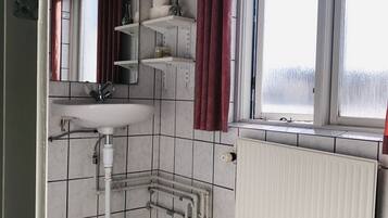 A bathroom with a white sink, mirror, and radiator. There are shelves with toiletries and a window with curtains.