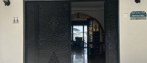 Entrada de un hotel con una gran puerta metálica ornamentada, un cartel arriba que indica el nombre del hotel y su año de fundación, y un pequeño letrero a la derecha.