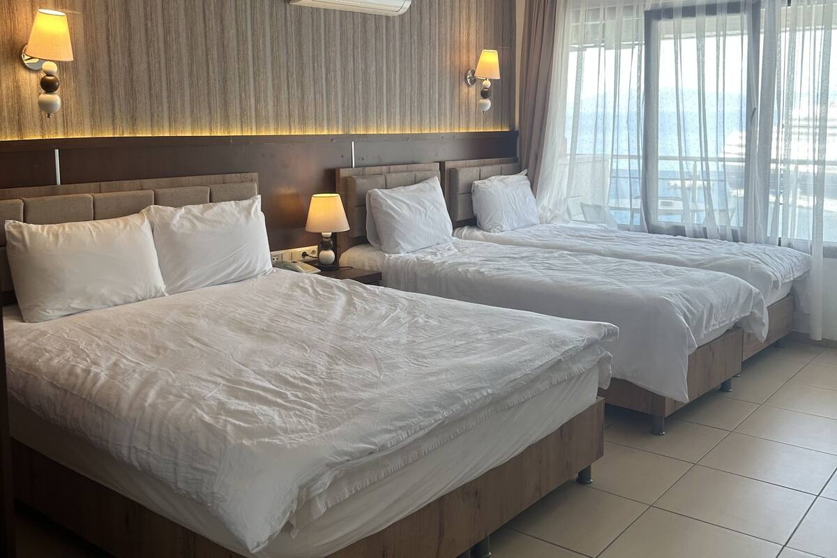 A hotel room with two beds, a wooden headboard, a wall-mounted air conditioner, and a window with sheer curtains.
