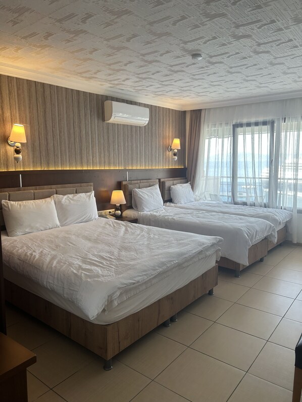 A hotel room with two beds, a wooden headboard, a wall-mounted air conditioner, and a window with sheer curtains.
