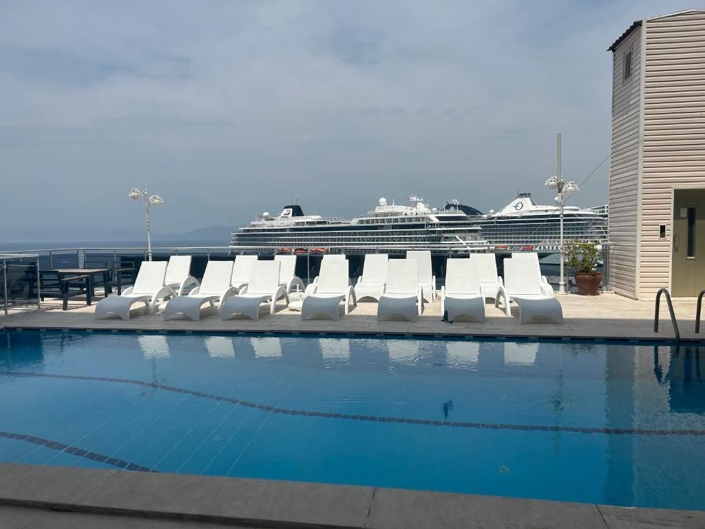 A pool area with lounge chairs and a view of a cruise ship.