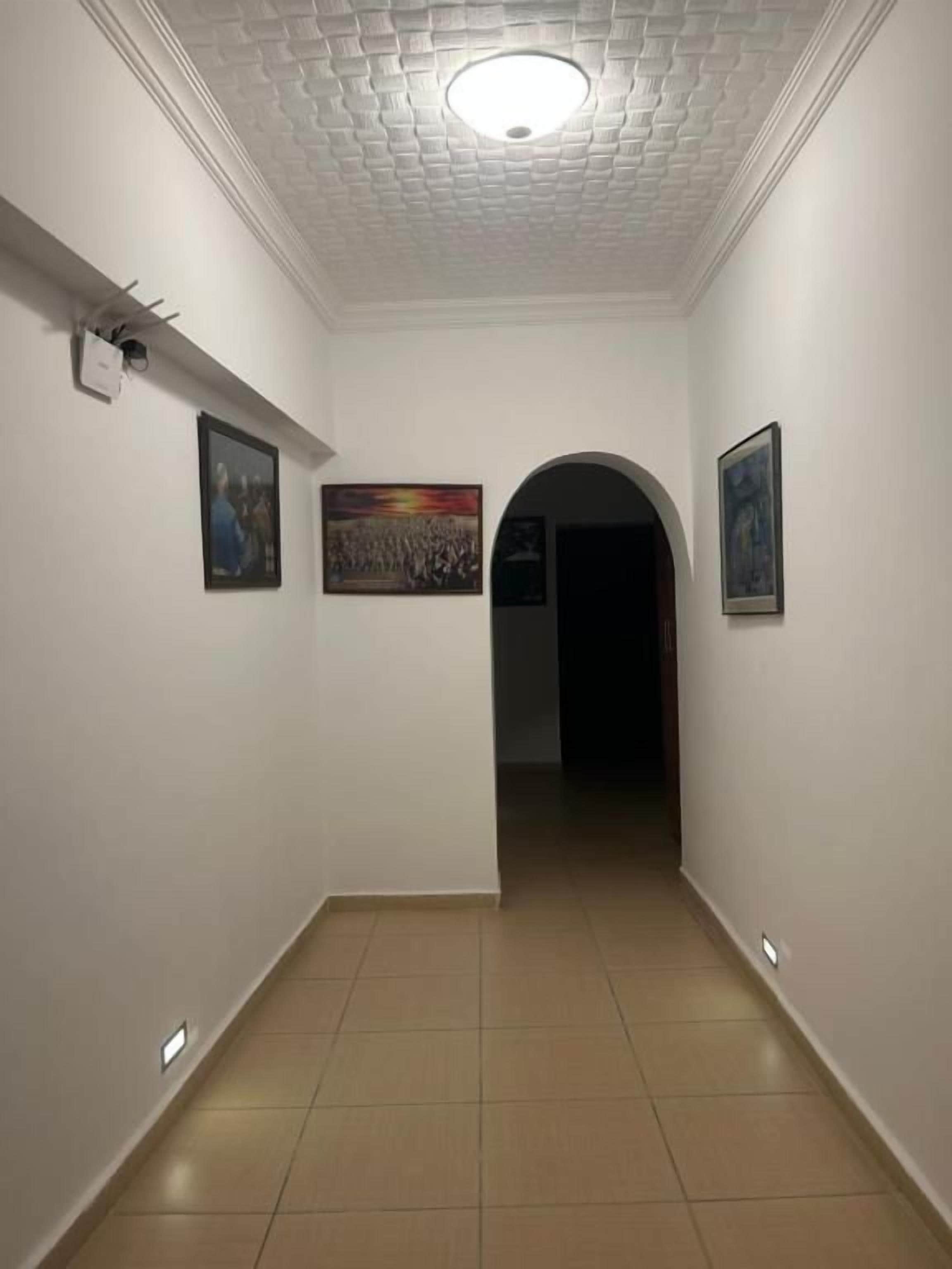 A hallway with white walls, a tiled floor, and framed pictures on the walls.