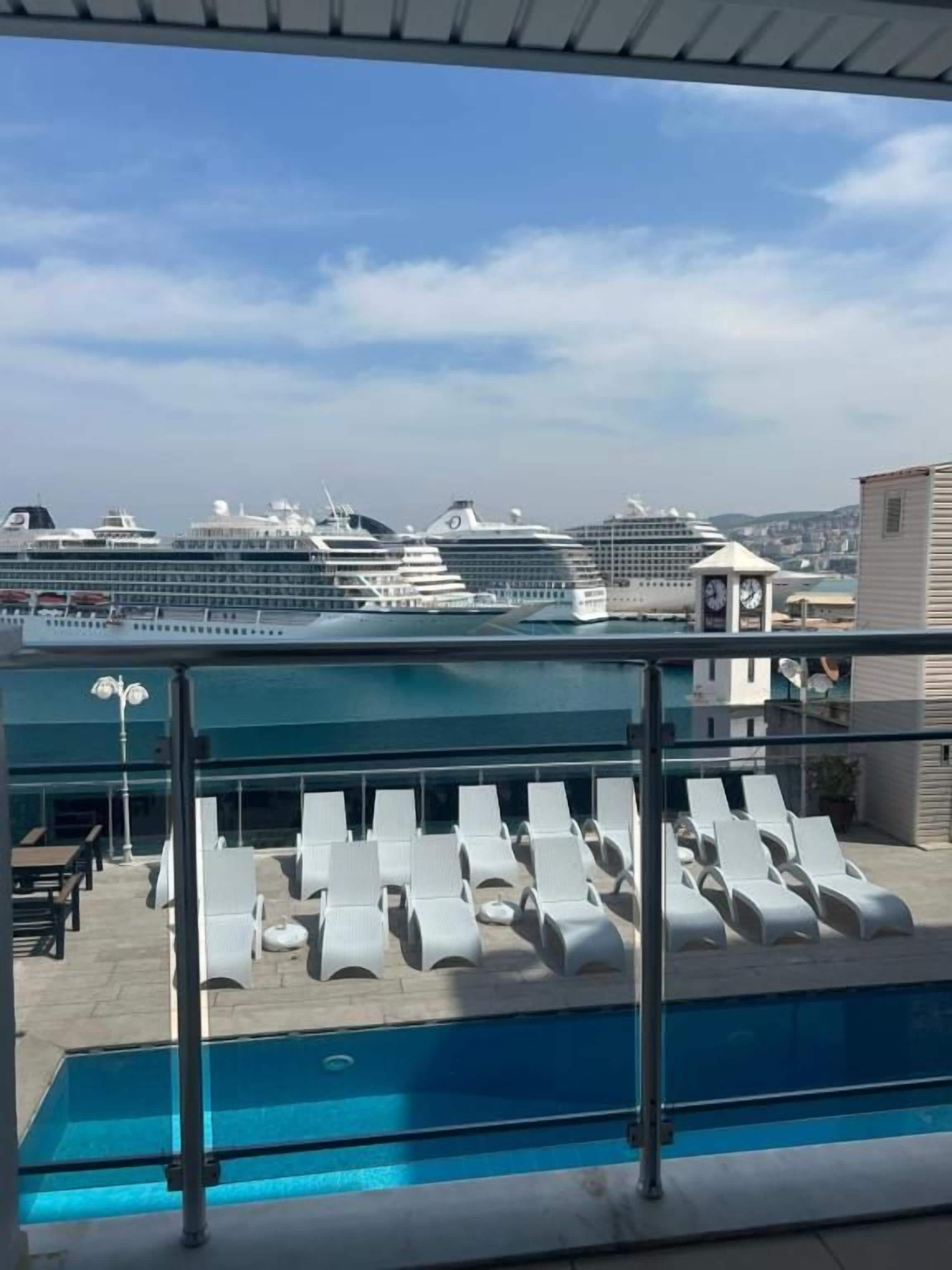 A pool area with lounge chairs and a view of cruise ships in the background.