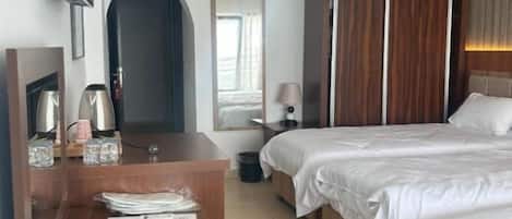 A hotel room with a wooden desk, a bed with white bedding, a wardrobe, and a television on the wall.