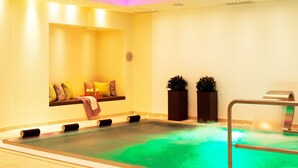 Un área de spa con piscina climatizada, asientos con cojines y dos plantas en macetas.