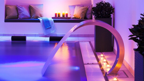 Un área de spa moderna con zona de estar, velas y fuente de agua.