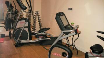 Un gimnasio en casa con dos elípticas, una bicicleta estática y una pequeña mesa con una botella de agua.