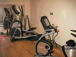 Un gimnasio en casa con dos elípticas, una bicicleta estática y una pequeña mesa con una botella de agua.