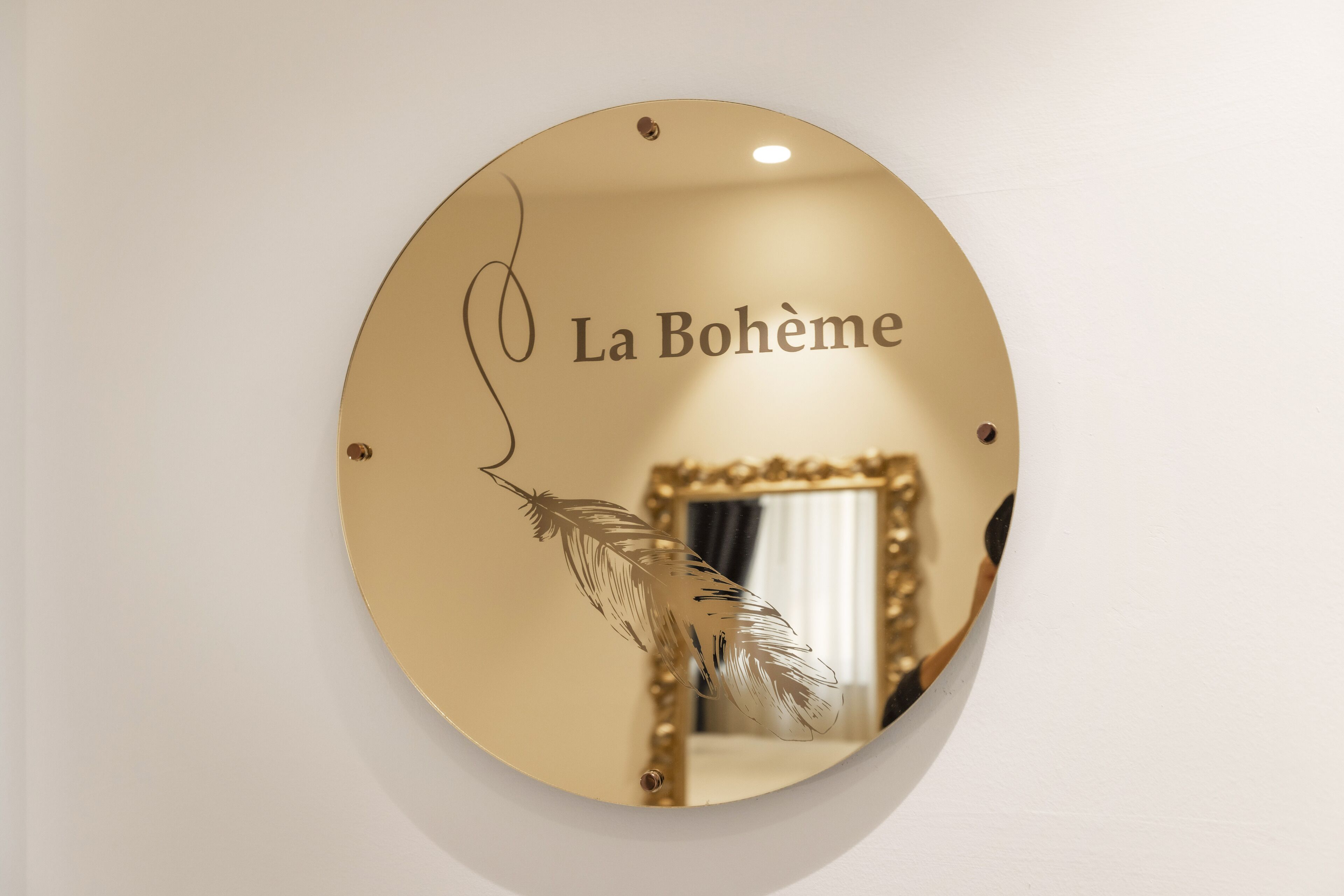 Uno specchio rotondo con l'iscrizione "La Bohème" e un disegno a piuma.