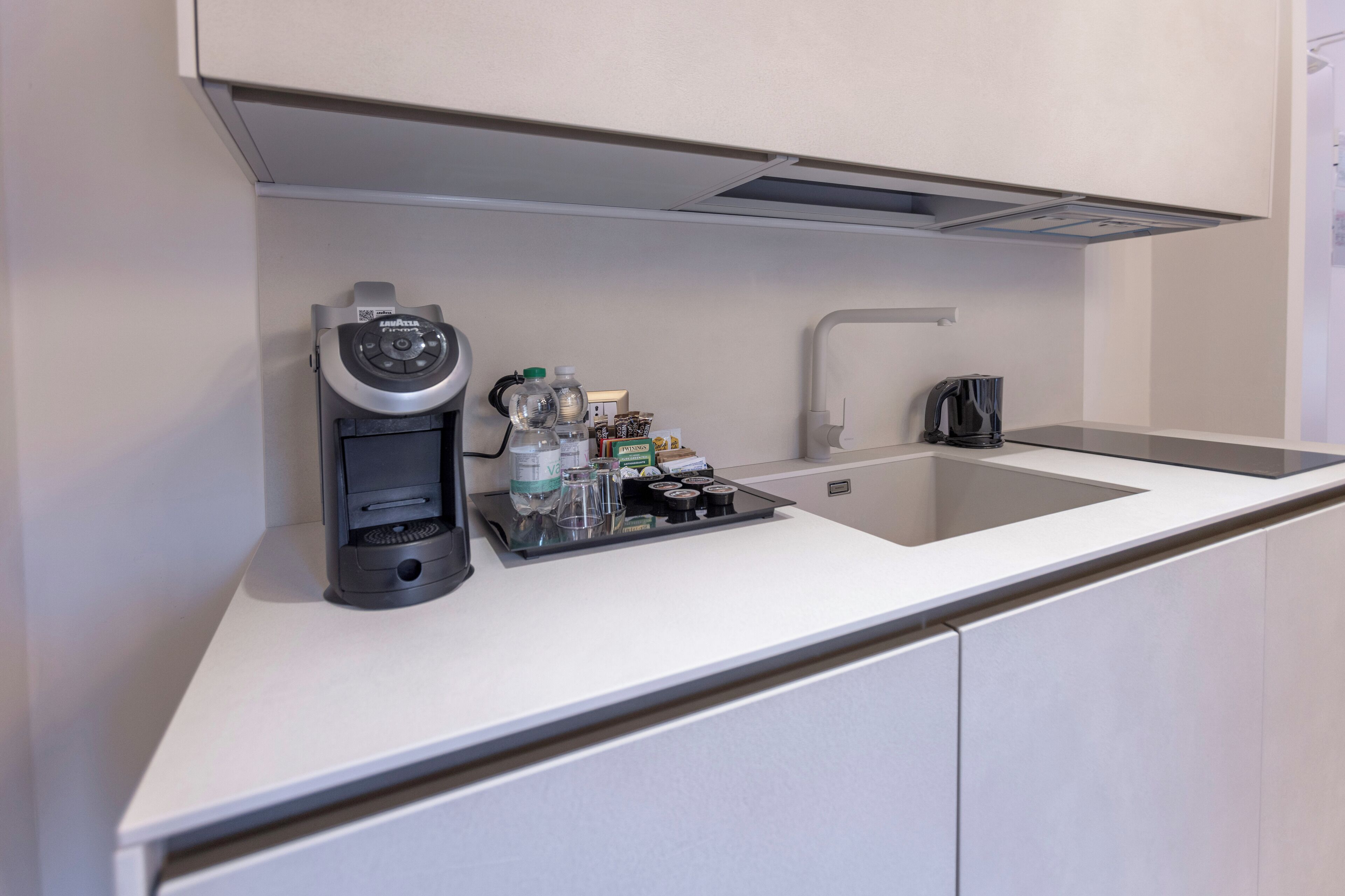 Una cocina moderna con cafetera integrada, hervidor y un escurreplatos con diversos objetos.