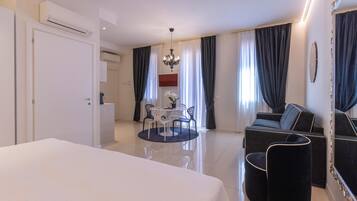 A hotel room with a bed, a dining table with chairs, a sofa, a mirror, and a chandelier.