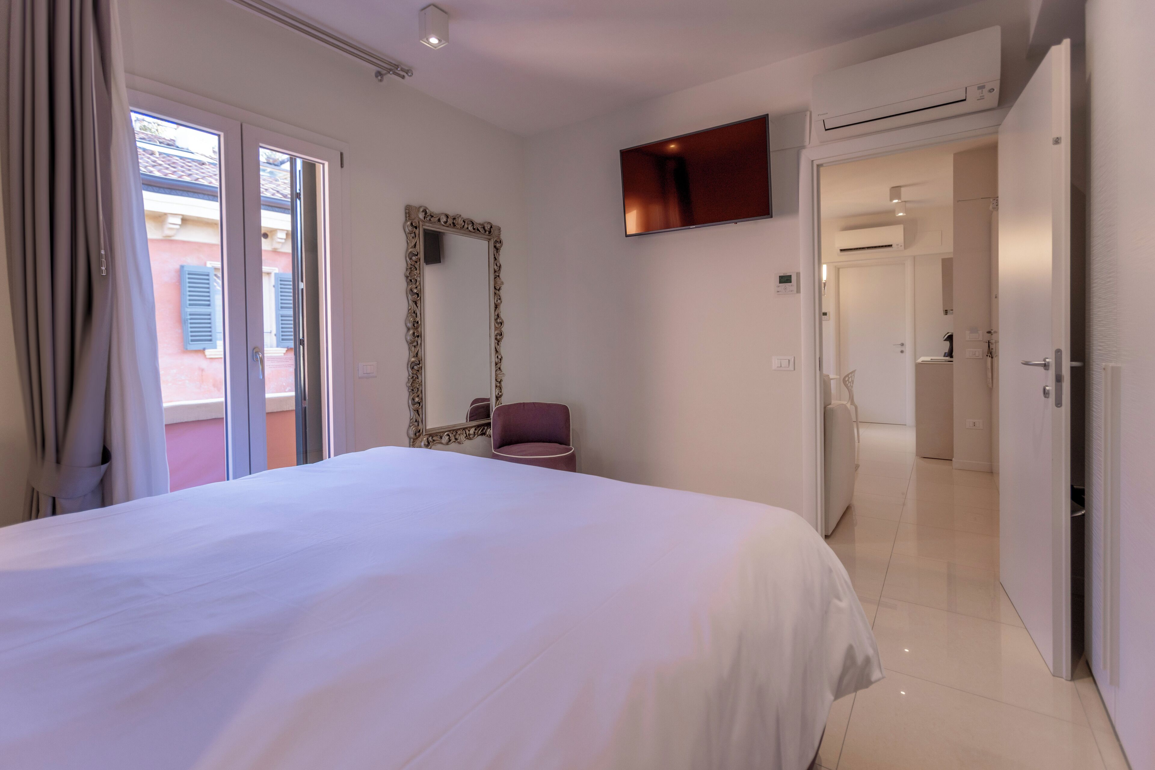 A hotel room with a large bed, a mirror, a TV, and a sliding door leading to a bathroom.