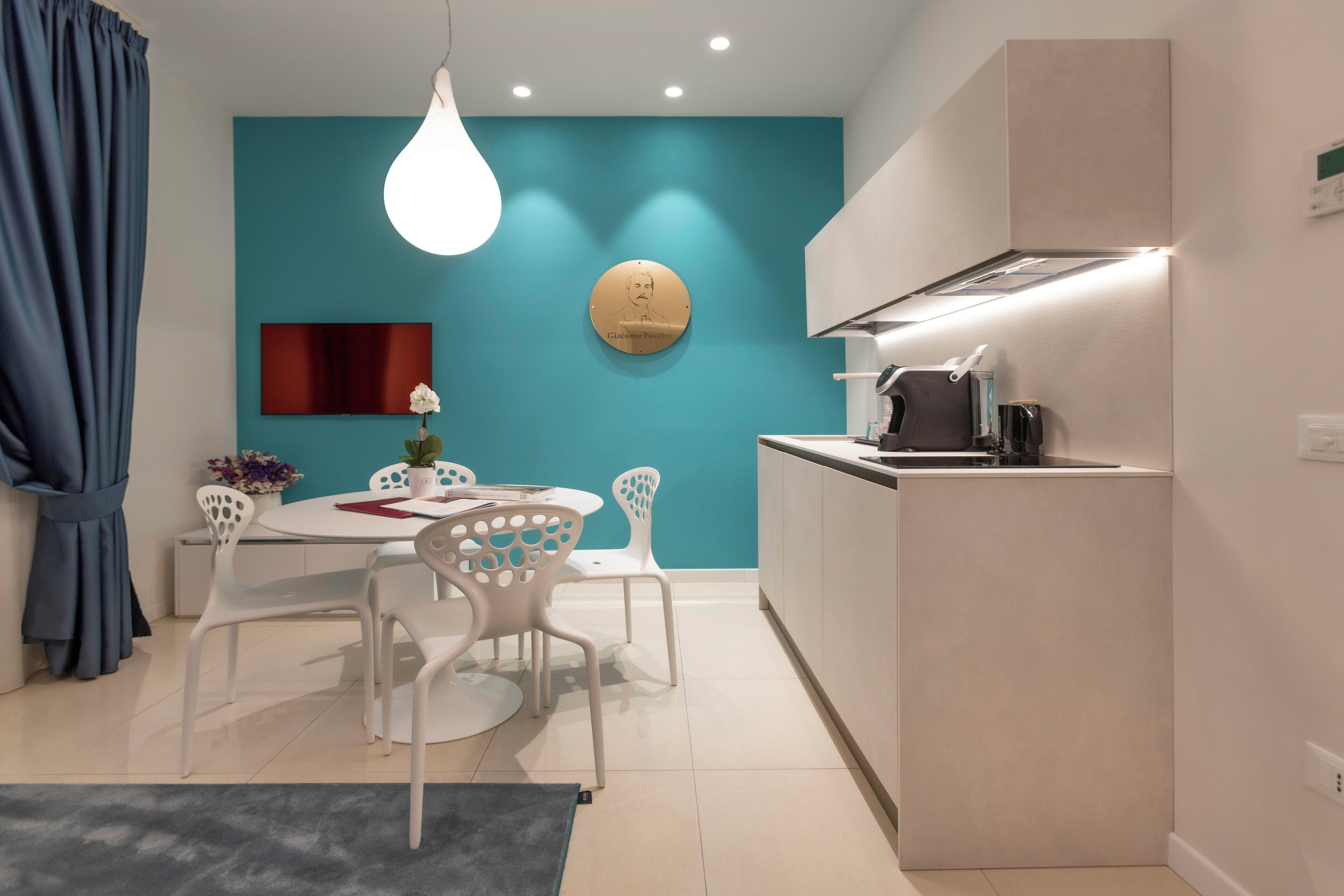 Una cocina moderna con una pared de acento color aguamarina, un plato decorativo redondo y una zona de comedor con sillas blancas y una mesa.