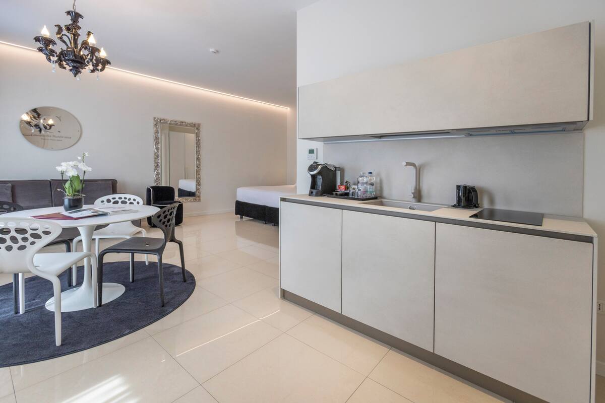 A modern kitchen with a dining area, including a white table with chairs, a chandelier, and a large mirror.