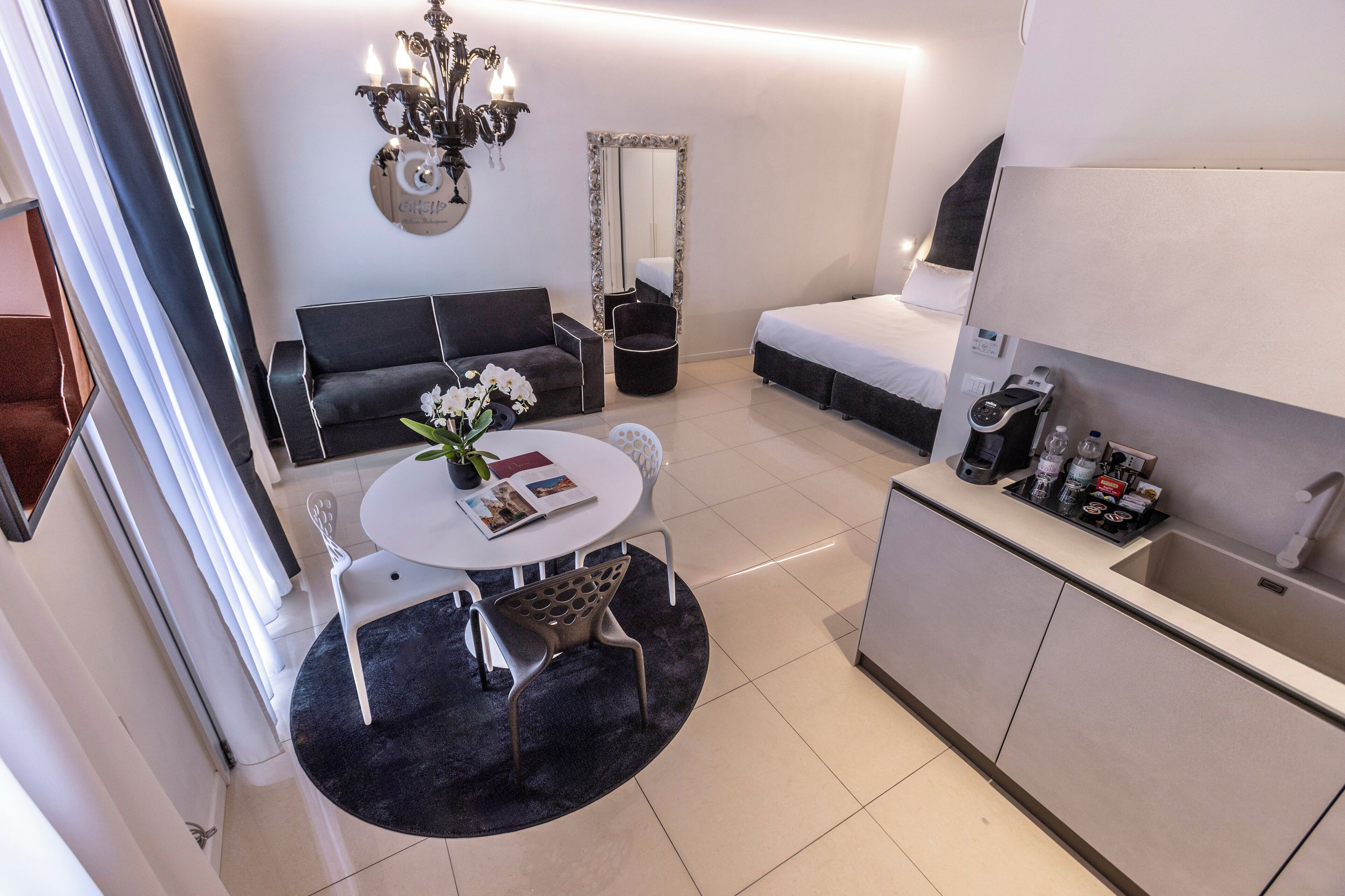 Ein modernes Hotelzimmer mit einer Couch, einem Esstisch mit Stühlen, einer kleinen Küchenzeile und einem großen Spiegel.