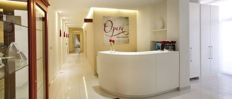 Zona de recepción de hotel con un mostrador blanco, un letrero que dice "Opera" y un diseño de interiores moderno.