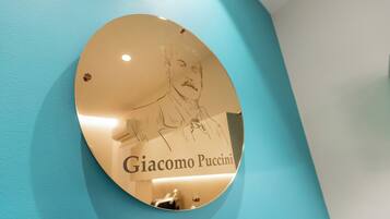 Una targa circolare con un ritratto e il nome Giacomo Puccini, fissata su una parete color acquamarina.
