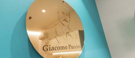 A circular plaque with a portrait and the name "Giacomo Puccini" mounted on a teal wall.