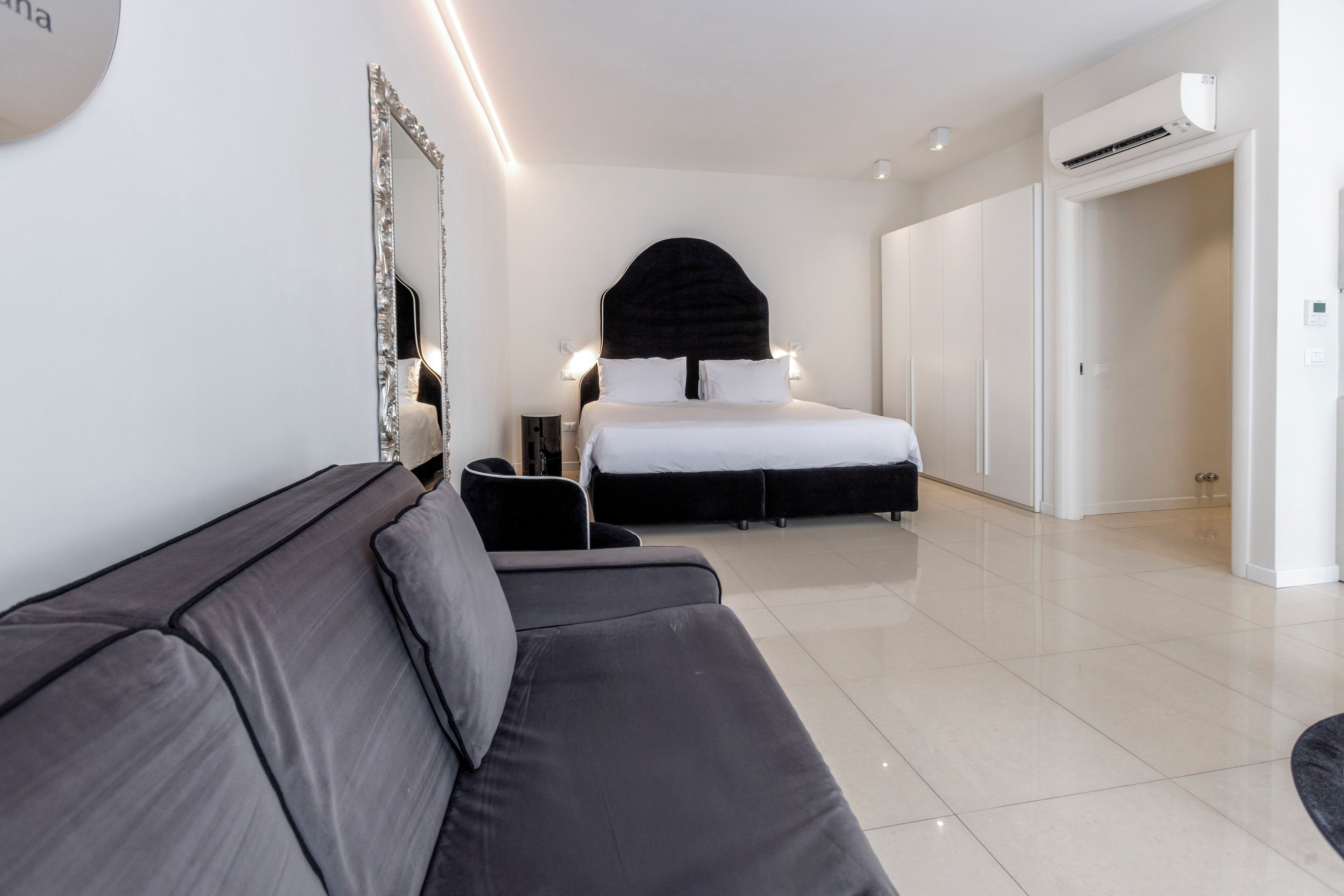 A modern hotel room with a large bed, a sofa, a mirror, and a wardrobe.
